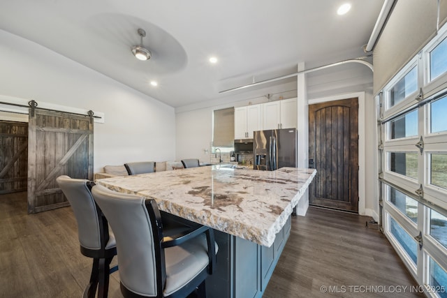 kitchen featuring dark wood-type flooring, a breakfast bar, white cabinetry, light stone counters, and stainless steel fridge with ice dispenser