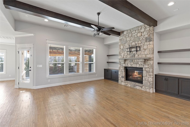 unfurnished living room with plenty of natural light, a stone fireplace, beam ceiling, and light hardwood / wood-style flooring