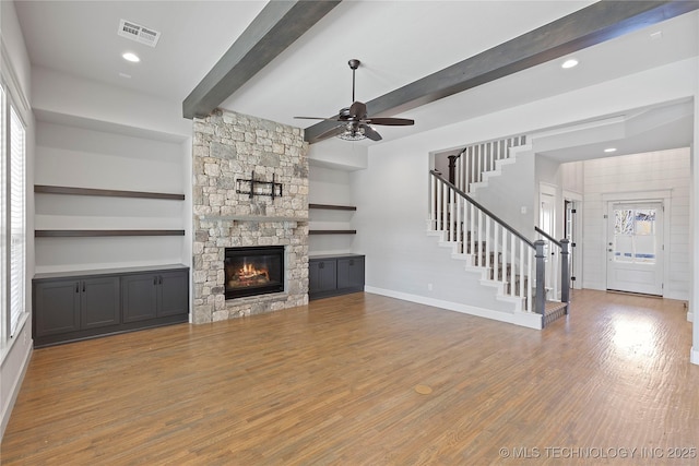 unfurnished living room with beam ceiling, a stone fireplace, ceiling fan, and hardwood / wood-style flooring