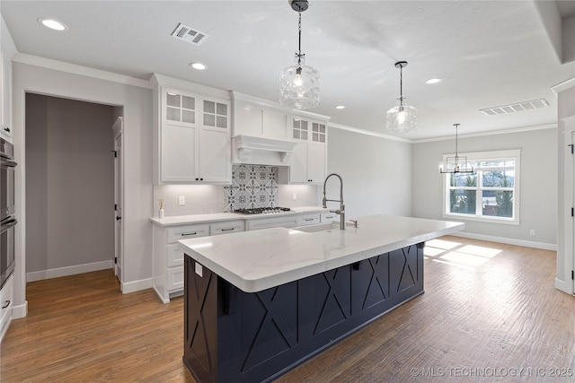 kitchen with sink, white cabinetry, a kitchen island with sink, light stone countertops, and stainless steel gas stovetop