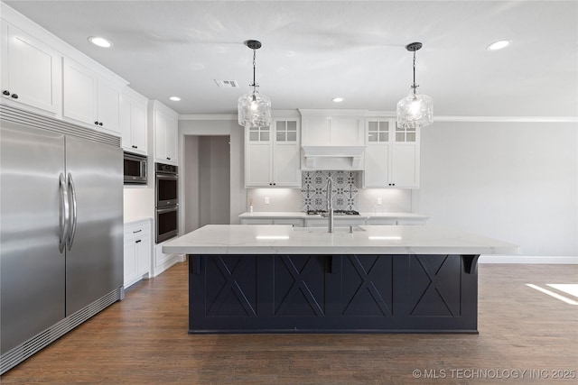 kitchen featuring dark hardwood / wood-style floors, built in appliances, a kitchen island with sink, and white cabinets