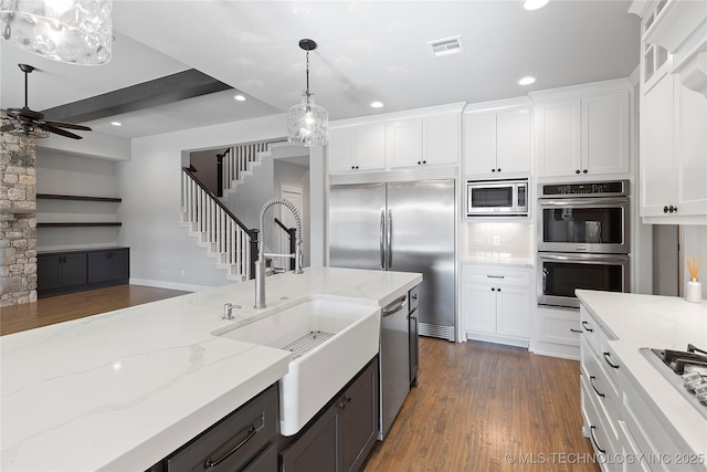 kitchen with light stone countertops, pendant lighting, built in appliances, and white cabinets