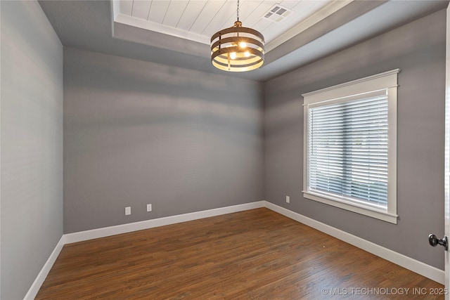 empty room featuring hardwood / wood-style flooring, a raised ceiling, and a notable chandelier