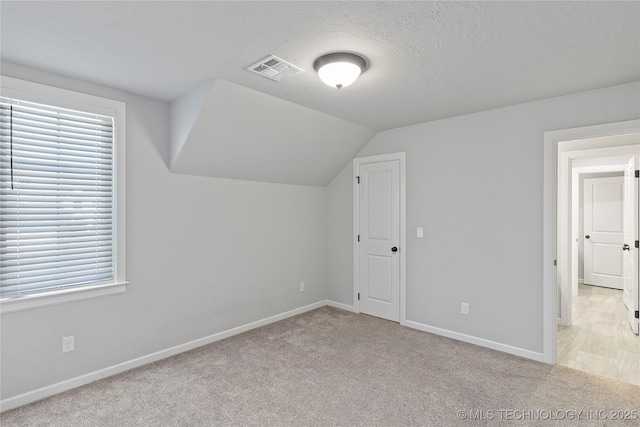 bonus room with light colored carpet, vaulted ceiling, and a textured ceiling