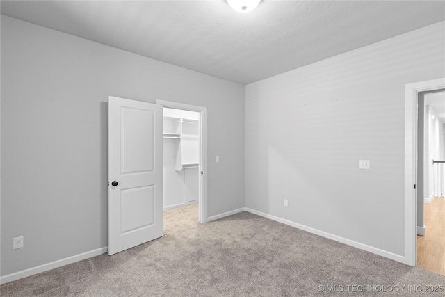 unfurnished bedroom with a spacious closet, light carpet, and a closet