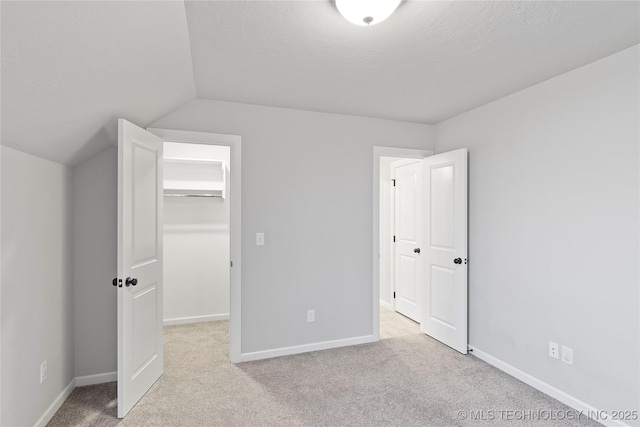 unfurnished bedroom with lofted ceiling, a textured ceiling, a walk in closet, light colored carpet, and a closet