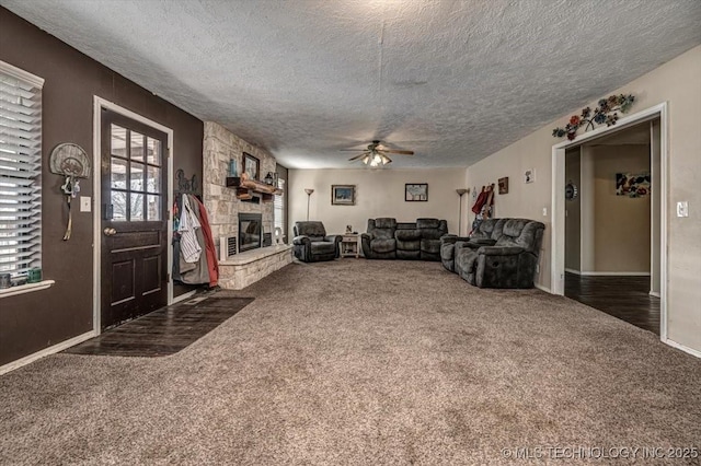 unfurnished living room featuring dark colored carpet, a stone fireplace, ceiling fan, and a textured ceiling