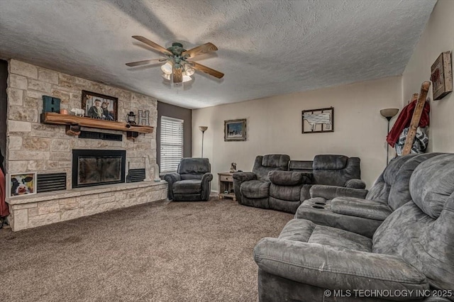 carpeted living room with ceiling fan, a stone fireplace, and a textured ceiling