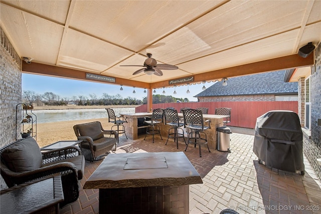 view of patio with a water view, grilling area, an outdoor bar, and ceiling fan