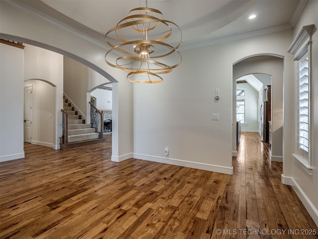 unfurnished dining area featuring an inviting chandelier, ornamental molding, and dark wood-type flooring