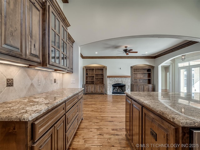 kitchen with light stone counters, light wood-type flooring, a kitchen island, ceiling fan, and a fireplace