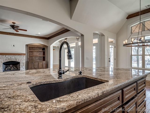 kitchen with pendant lighting, sink, a stone fireplace, light stone countertops, and built in shelves