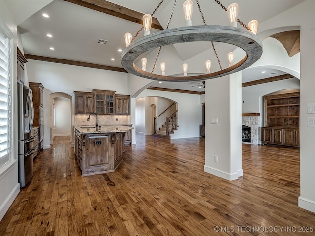 kitchen featuring a fireplace, stainless steel refrigerator, sink, decorative backsplash, and a kitchen island with sink