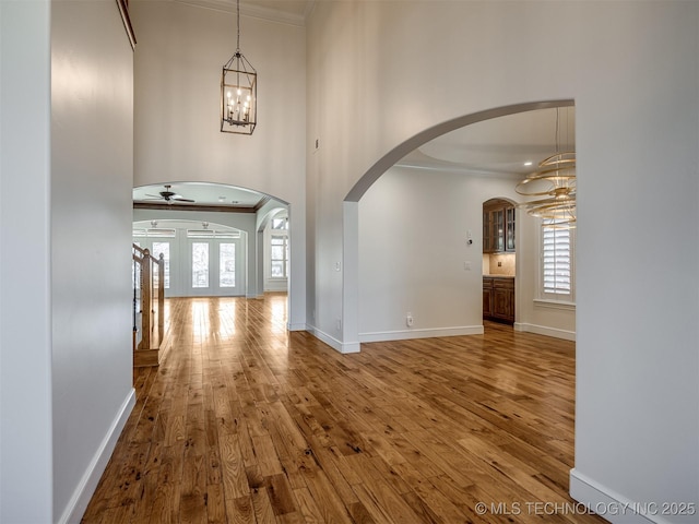 foyer with ceiling fan with notable chandelier, wood-type flooring, and ornamental molding