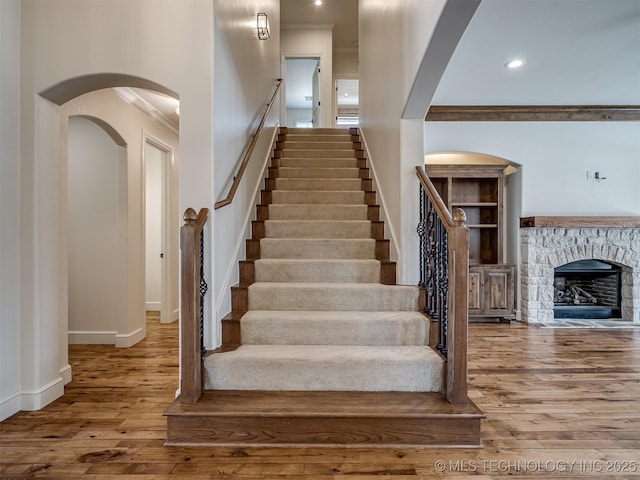 stairs featuring crown molding, a stone fireplace, and hardwood / wood-style floors