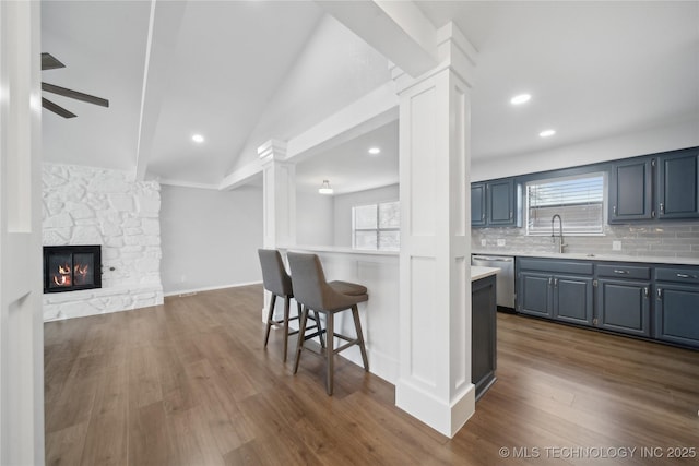 kitchen featuring lofted ceiling, sink, backsplash, a fireplace, and stainless steel dishwasher