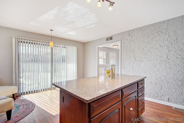 kitchen with light stone counters, dark hardwood / wood-style flooring, a center island, and hanging light fixtures