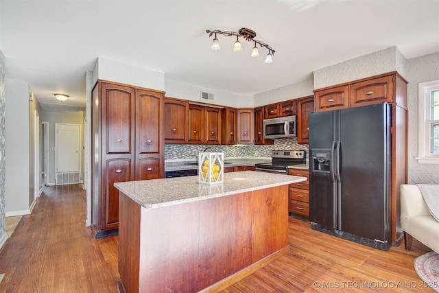 kitchen with light wood-type flooring, backsplash, a kitchen island, and appliances with stainless steel finishes