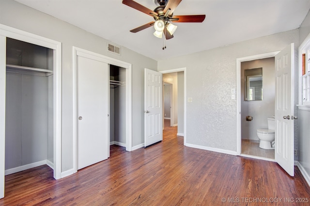 unfurnished bedroom with multiple closets, dark hardwood / wood-style flooring, ceiling fan, and ensuite bath