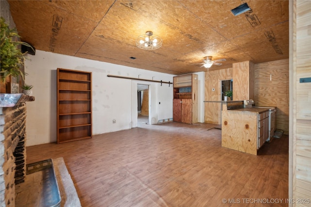 unfurnished living room featuring wood walls, dark hardwood / wood-style flooring, ceiling fan, and a barn door