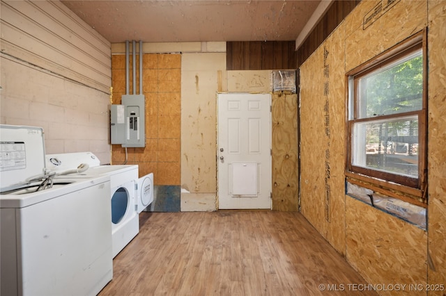 washroom with light wood-type flooring, washing machine and clothes dryer, wood walls, and electric panel