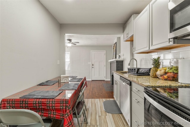 kitchen with light wood-type flooring, light stone counters, decorative backsplash, appliances with stainless steel finishes, and a ceiling fan