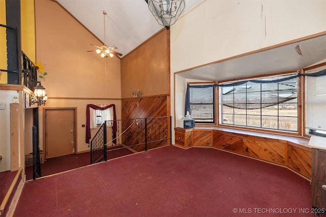 interior space with high vaulted ceiling, carpet, wood walls, and ceiling fan