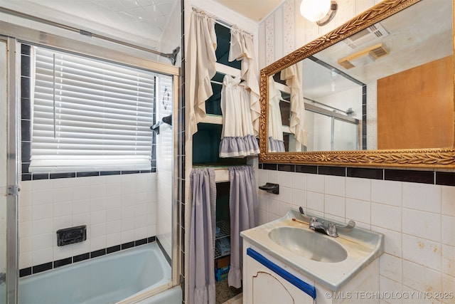 bathroom featuring vanity, bath / shower combo with glass door, and tile walls