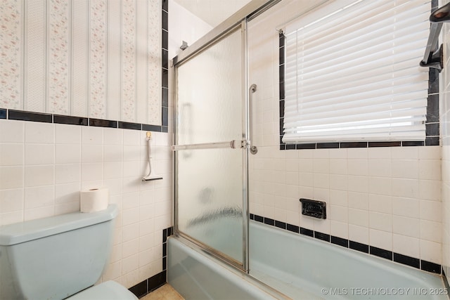 bathroom featuring toilet and shower / bath combination with glass door