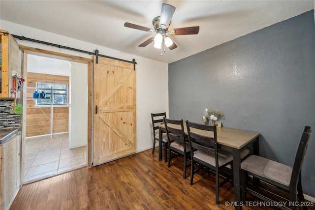 dining area with hardwood / wood-style flooring, a barn door, and ceiling fan