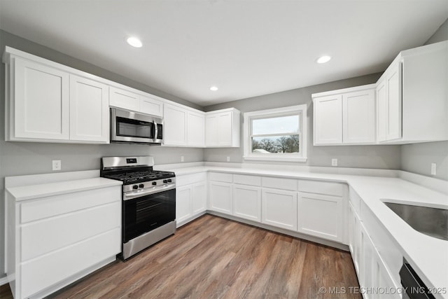 kitchen with stainless steel appliances, white cabinetry, sink, and hardwood / wood-style floors