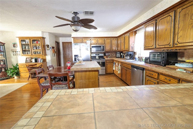 kitchen with a center island, sink, light hardwood / wood-style flooring, stainless steel appliances, and tile countertops