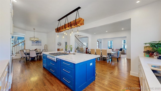 kitchen featuring pendant lighting, blue cabinetry, white cabinets, a center island with sink, and stainless steel gas stovetop