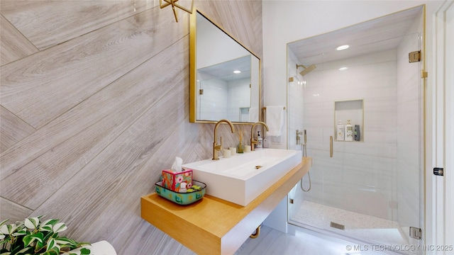 bathroom featuring a shower with shower door, sink, and tile walls