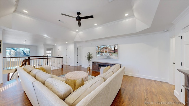 living room with wood-type flooring, ornamental molding, ceiling fan, and a tray ceiling