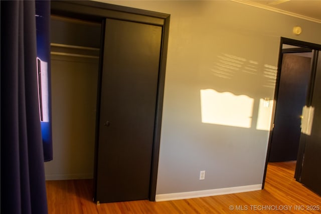 unfurnished bedroom with wood-type flooring, ornamental molding, and a closet