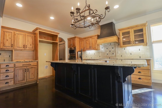 kitchen featuring crown molding, light stone countertops, custom range hood, and a center island with sink