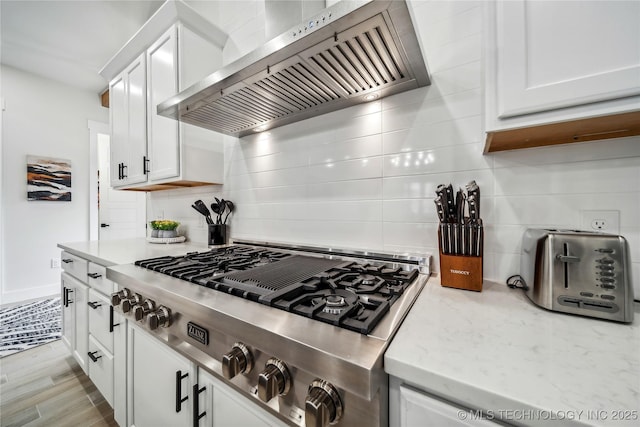 kitchen with white cabinetry, backsplash, stainless steel gas stovetop, and wall chimney exhaust hood