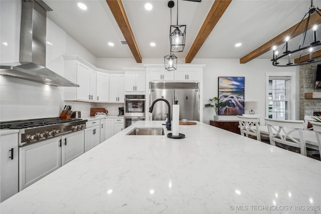 kitchen featuring wall chimney range hood, beamed ceiling, stainless steel appliances, light stone countertops, and white cabinets