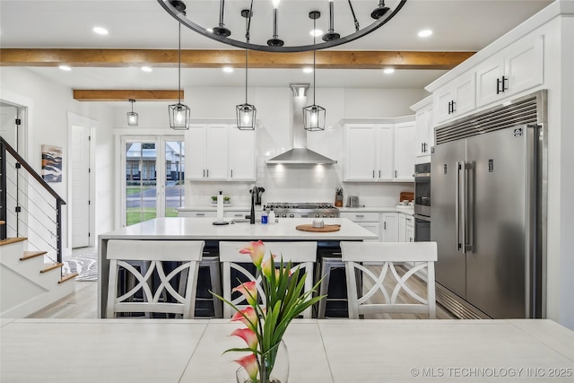 kitchen with hanging light fixtures, stainless steel appliances, extractor fan, white cabinets, and a kitchen bar