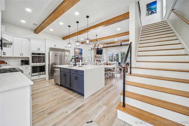 kitchen with appliances with stainless steel finishes, pendant lighting, white cabinetry, a kitchen island with sink, and light wood-type flooring