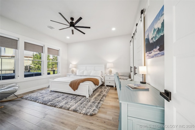 bedroom with light hardwood / wood-style floors, a barn door, and ceiling fan