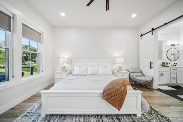 bedroom with multiple windows, a barn door, ceiling fan, and light hardwood / wood-style floors