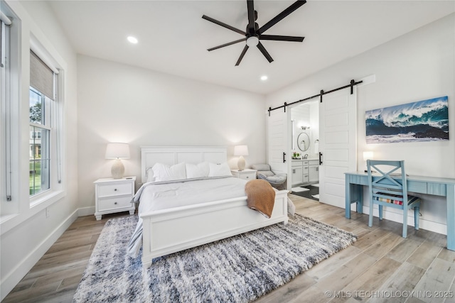 bedroom featuring a barn door, connected bathroom, ceiling fan, and light hardwood / wood-style flooring