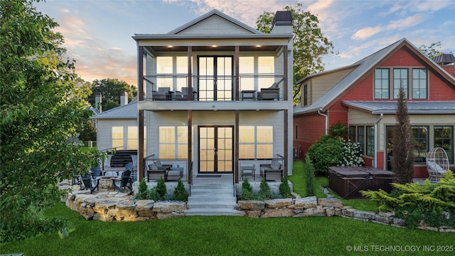 back house at dusk featuring a patio, a balcony, a lawn, a hot tub, and a sunroom