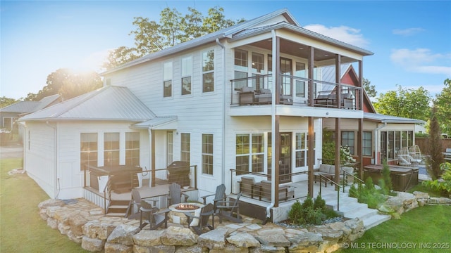 rear view of property featuring a sunroom, a patio, a balcony, and an outdoor fire pit