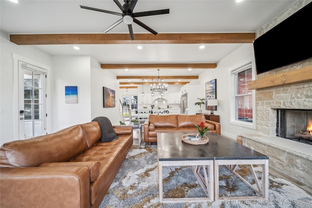 living room with beam ceiling, a stone fireplace, and ceiling fan with notable chandelier