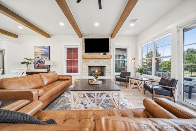 living room with beam ceiling, a stone fireplace, light hardwood / wood-style flooring, and ceiling fan