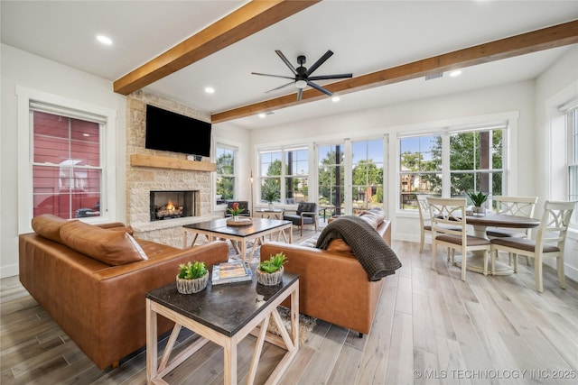 living room featuring beamed ceiling, ceiling fan, a fireplace, and light hardwood / wood-style floors