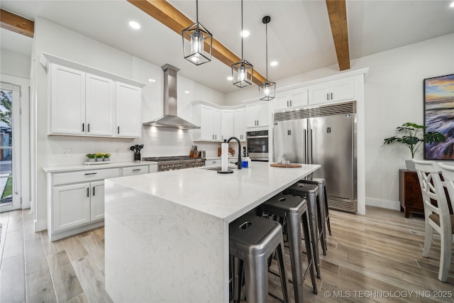 kitchen with beamed ceiling, sink, white cabinets, stainless steel appliances, and wall chimney exhaust hood